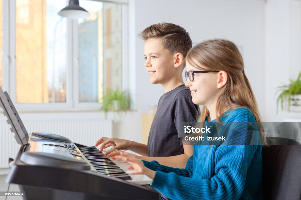 Pre-adolescent friends playing piano in class Smiling boy and girl playing piano in music class. Pre-adolescent friends are learning music in training class. They are in casuals at conservatory. Piano Stock Photo