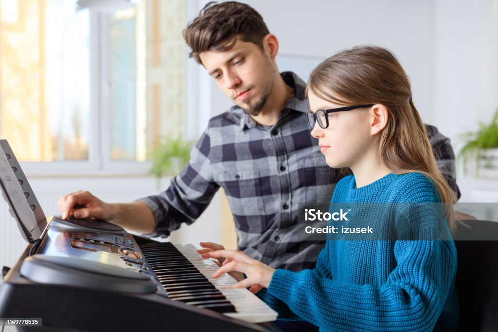 Teacher with student playing piano in class Pianist looking at female student while playing piano. Pre-adolescent girl is learning music in conservatory. They are in training class. Piano Stock Photo