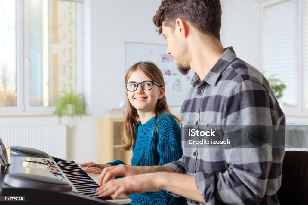 Trainer teaching piano to girl in class Male teacher playing piano with pre-adolescent girl. Student is learning music from instructor in training class. They are at conservatory. 10-11 Years Stock Photo
