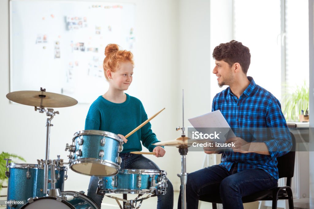 Female drummer looking while practicing by teacher Smiling music teacher holding sheet looking at female student. Pre-adolescent drummer is practicing by instructor. They are in conservatory. 12-13 Years Stock Photo