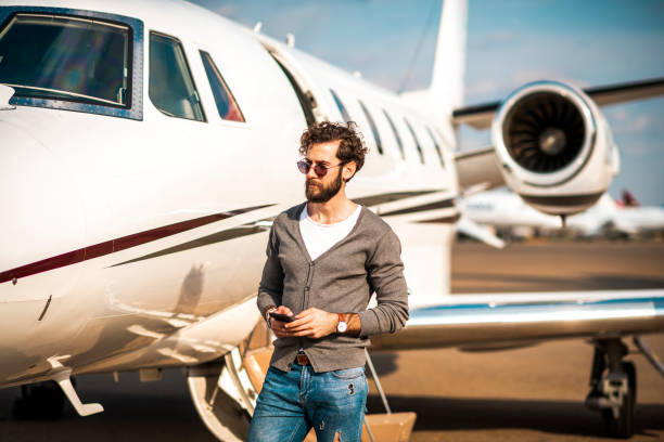 istock Young rich man using a smart phone while disembarking outside of the private jet parked on a runway 1149786370