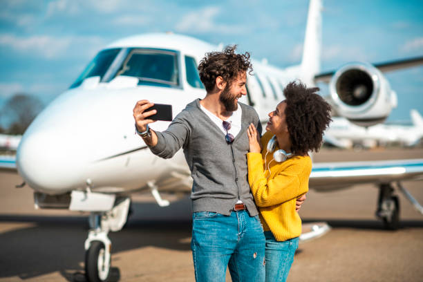 istock Rich young couple looking at each other while taking a selfie on a mobile phone in front of a private jet parked on an airport tarmac 1149788468