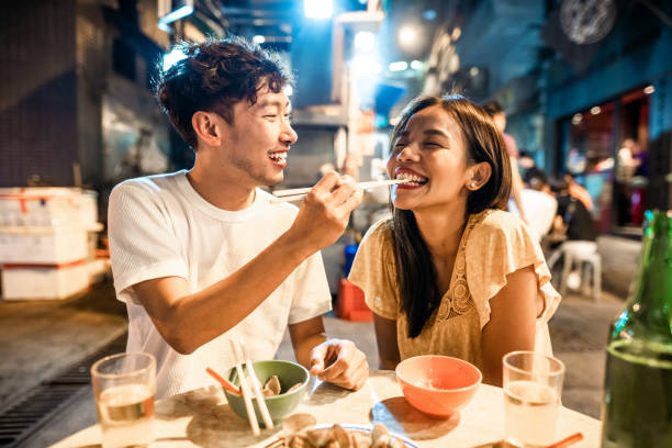 pareja asiática disfrutando de la comida callejera en hong kong - asian cuisine fotografías e imágenes de stock