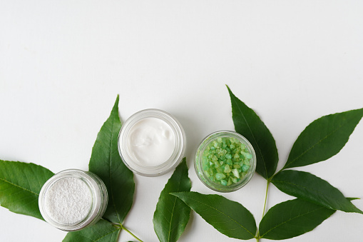 natural cosmetics cream, sea salt with leaves for homemade bath spa white table background for text top view mock up
