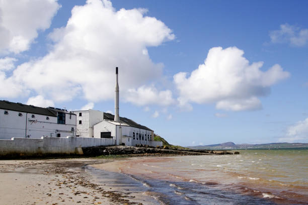 Bowmore, Isle of Islay, Scotland, United Kingdom - May 02, 2018: The Bowmore Whisky Distillery Bowmore, Isle of Islay, Scotland, United Kingdom - May 02, 2018: The Bowmore Whisky Distillery seen from the beach next to the building bowmore whisky stock pictures, royalty-free photos & images