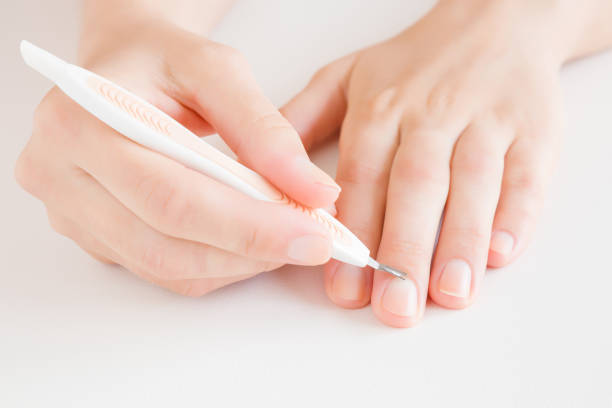 istock Woman's hand removing nail cuticle with pusher stick on light gray table. Care about dry, overgrown cuticle. Front view. Closeup. 1149811479