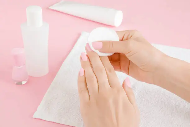 Photo of Woman's hand removing pink nail polish with white cotton pad on towel. Closeup.