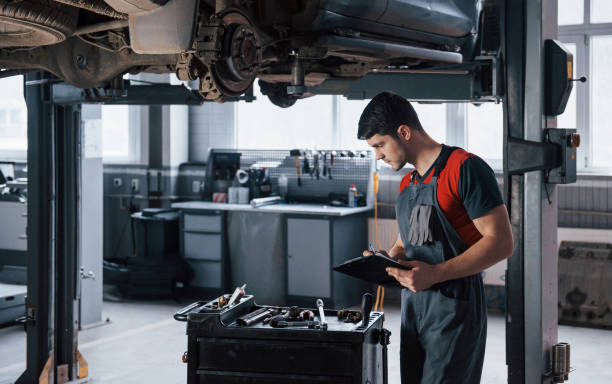 istock Nice looking autosalon. Man at the workshop in uniform using notepad for his job for fixing broken car 1149814925