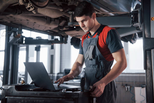 istock Silver colored device. Man at the workshop in uniform using laptop for his job for fixing broken car 1149815212