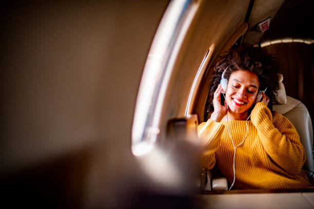 joven mujer de moda sentada en un avión privado con los ojos cerrados mientras escucha música a través de auriculares - status symbol audio fotografías e imágenes de stock