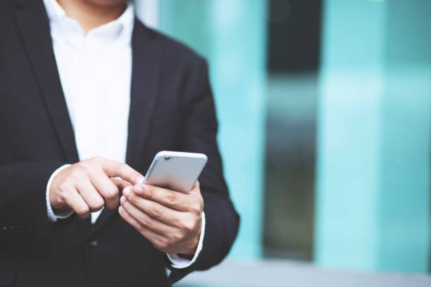 istock close up hand Business man working using phone device while standing in front of in an office building overlooking the city. 1149819942