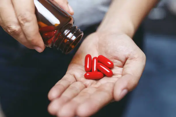 Photo of close up man hand holding a medicine, with pours the pills vitamin out of the bottle. Caring for the health care