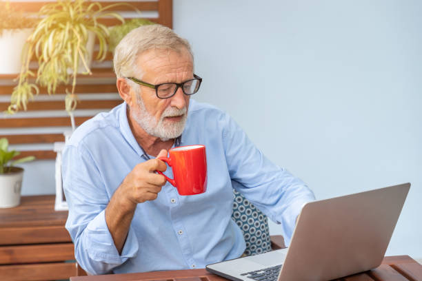 istock Senior man executive with white hair using computer laptop watching movie at home drinking coffee 1149824911
