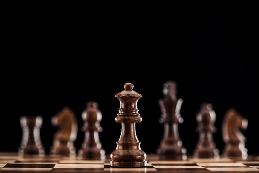 selective focus of brown wooden queen on chessboard isolated on black
