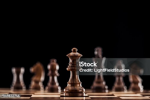 istock selective focus of brown wooden queen on chessboard isolated on black 1149832746