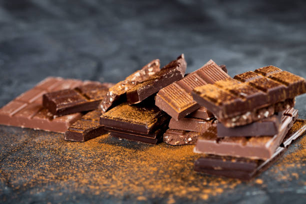 istock Broken chocolate stacked on black background. Chocolate bar pieces heap witn cinnamon powder. 1149837545