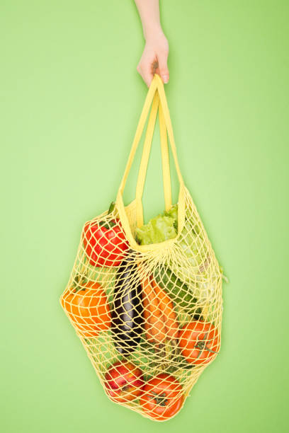istock partial view of woman holding string bag with vegetables on light green 1149839828