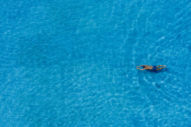 top view of happy man is relaxing and enjoy swimming in the swimming pool of the luxury hotel and resort with warm beautiful sunlight at the summertime with copy space. summer holiday vacation idyllic. travel and hotel concept - blue water swimming pool sports and fitness imagens e fotografias de stock