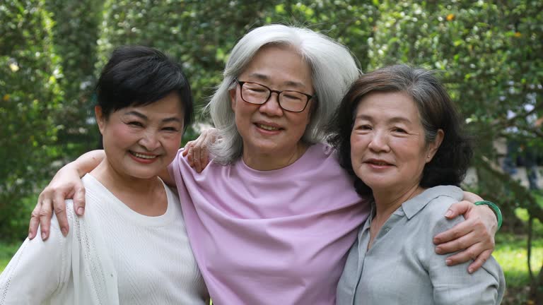 Three Elderly Taiwanese Friends Embracing While Out At The Park