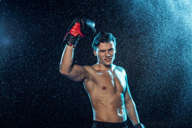istock Smiling boxer standing with hand up under water drops on black 1149876659