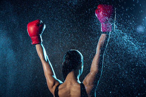 Back view of boxer in red boxing gloves showing yes gesture on black