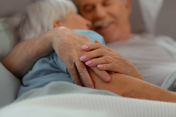Close-up of aged nice-appealing good-looking loving aged couple holding hands Holding hands. Close-up picture of aged nice-appealing good-looking loving aged couple holding hands while lying in the bed old man pajamas photos stock pictures, royalty-free photos & images
