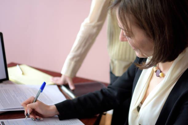 istock young smartly dressed lady helps another young lady to work with documents, fill forms and sign 1149888104