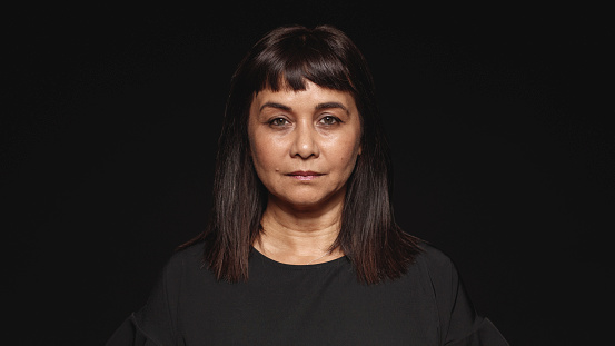 Close up of middle aged woman looking at camera. Woman in  black dress isolated on black background.