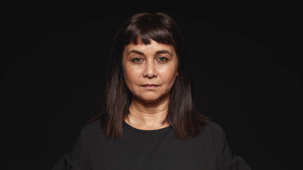 Portrait of woman Close up of middle aged woman looking at camera. Woman in black dress isolated on black background. grave stock pictures, royalty-free photos & images