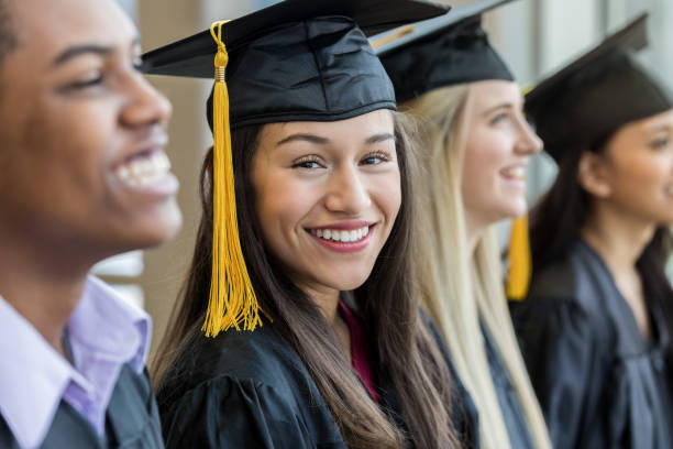 Confident graduating seniors Beautiful Hispanic female high school graduate smiles at the camera. She is surrounded by classmates. high school student photos stock pictures, royalty-free photos & images