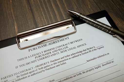 Clipboard with purchase agreement and pen on wooden desk background