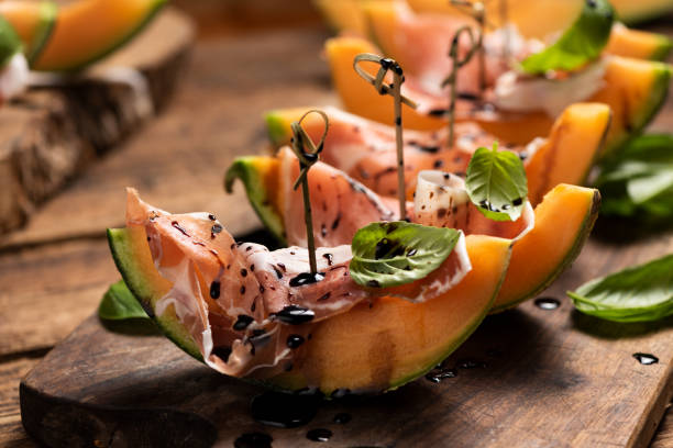 istock Sliced melon with ham and basil leaves, served on a wood chopping board 1149906161