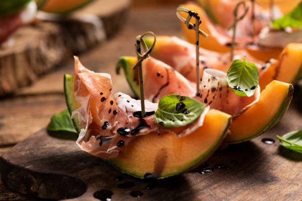 istock Sliced melon with ham and basil leaves, served on a wood chopping board 1149906273