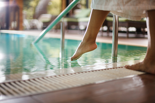 Mujer en bata de baño sumergiendo los pies en la piscina photo