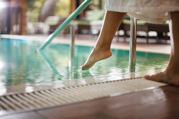 femme dans le peignoir plongeant des orteils dans la piscine - health spa swimming pool relaxation indoors photos et images de collection