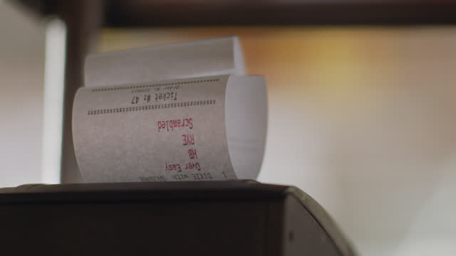 CU of an order ticket printing from a receipt printer in a busy commercial kitchen