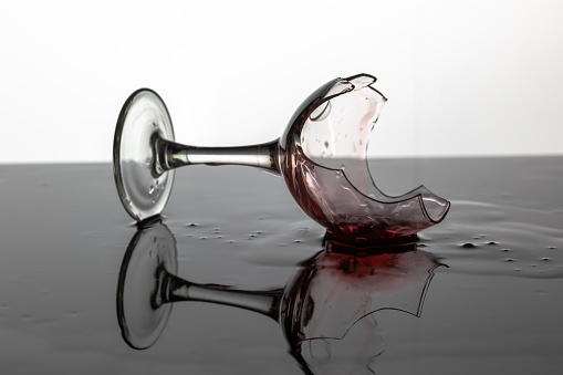 Broken wine glass with red wine which is laying on the wet surface. White background