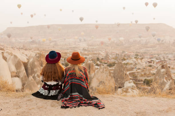 istock Traveling women wearing authentic boho chic style poncho, sweeter and hats looking on air ballons in sky in Cappadocia valley. Travel and wanderlust concept. Copy space background. 1149955314