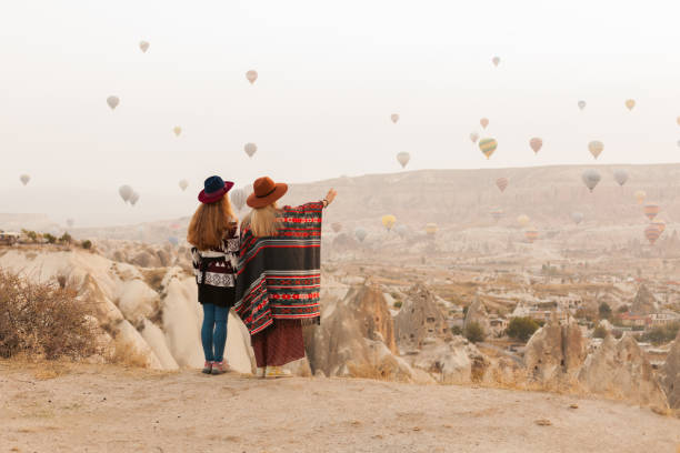 istock Traveling women wearing authentic boho chic style poncho, sweeter and hats looking on air ballons in sky in Cappadocia valley. Travel and wanderlust concept. Copy space background. 1149955320