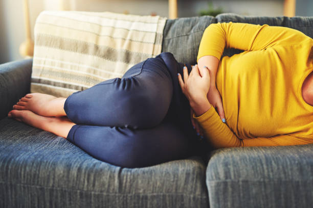 Do I need to get this checked out? Cropped shot of a woman suffering from stomach cramps on the sofa at home irritable bowel syndrome stock pictures, royalty-free photos & images