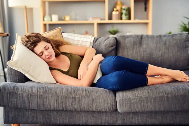 Shot of a young woman suffering from stomach cramps on the sofa at home