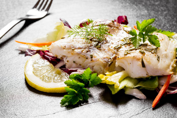 faixa grelhada do bacalhau com a salada na placa preta da ardósia - cod fillet fried prepared fish - fotografias e filmes do acervo