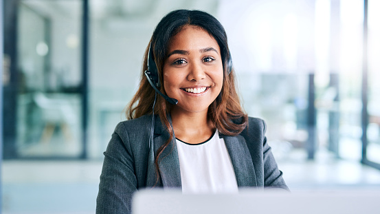 Shot of a young woman using a headset and laptop in a modern office