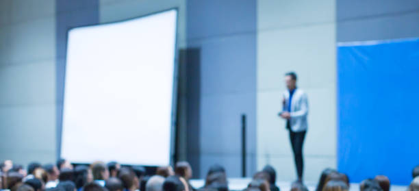istock Blurred seminar presenter at corporate conference giving speech. Speaker giving lecture to business audience. Defocused executive manager leading discussion in hall during company training event. 1150023398