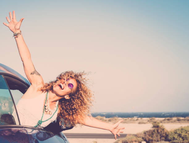 libertà e viaggi felice ridere concetto di persone con bella giovane donna caucasica fuori dall'auto godendosi il luogo di destinazione aprendo le braccia e gridando libero - oceano sullo sfondo e sole - spensieratezza foto e immagini stock