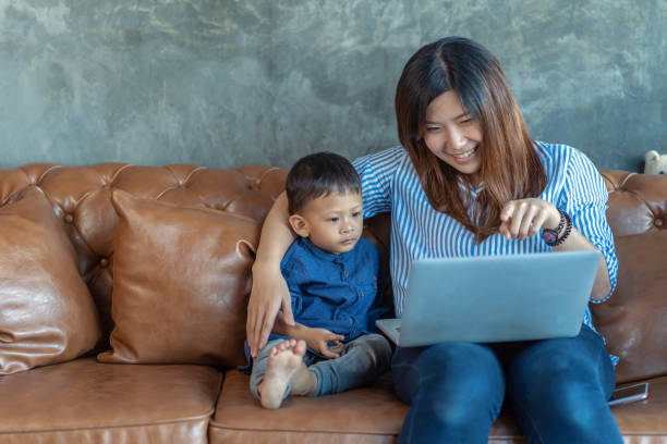 asiatique seule maman avec fils sont à la recherche de dessin animé ensemble via ordinateur portable de la technologie lorsque vous vivez dans la maison de loft pour l’auto-apprentissage ou l’école à la maison, famille et concept de mère célibata - brown boy photos et images de collection