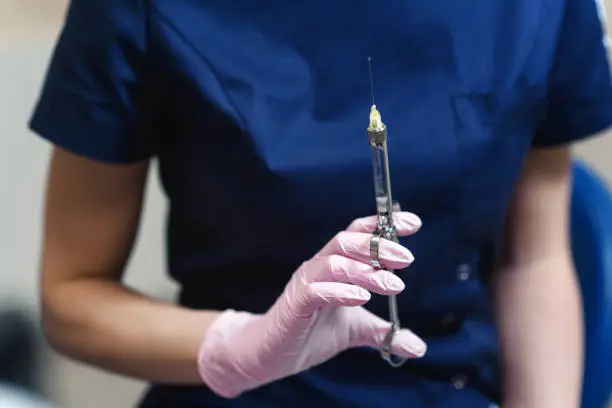 Doctor holding in her dentist's hand carpool syringe for local anesthesia on background isolated