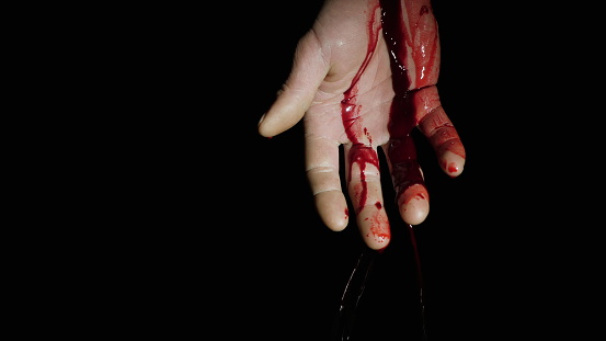 On the human hand, natural blood flows down against a dark background. Close-up