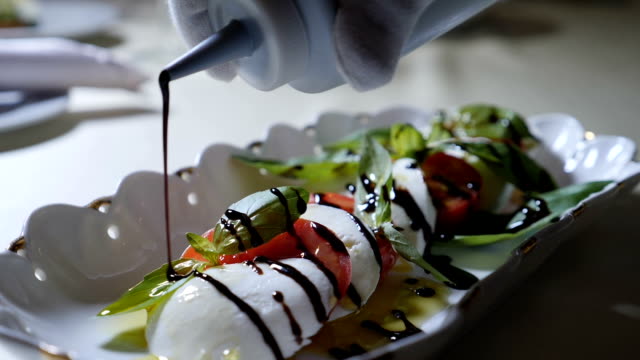 Food video. Healthy food and vegetarian concept. Close up of Pouring vinegar over caprese salad. Italian caprese salad with Mozzarella cheese. Slow motion