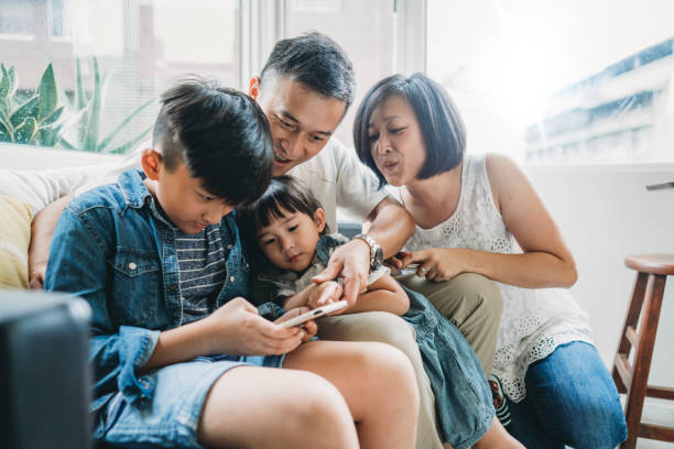семья с помощью мобильного телефона вместе сидит на диване дома - video game family child playful стоковые фото и изображения